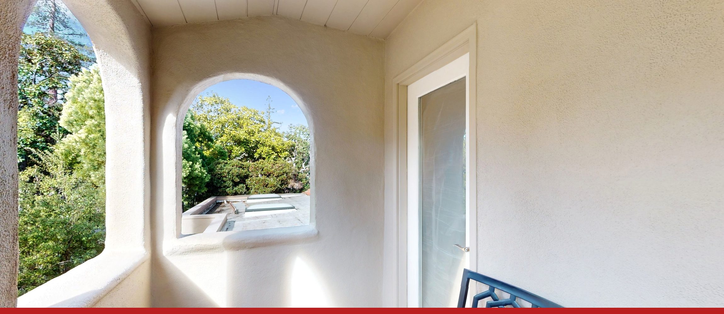 An arched opening in a stucco wall, looking out into a tree in daylight