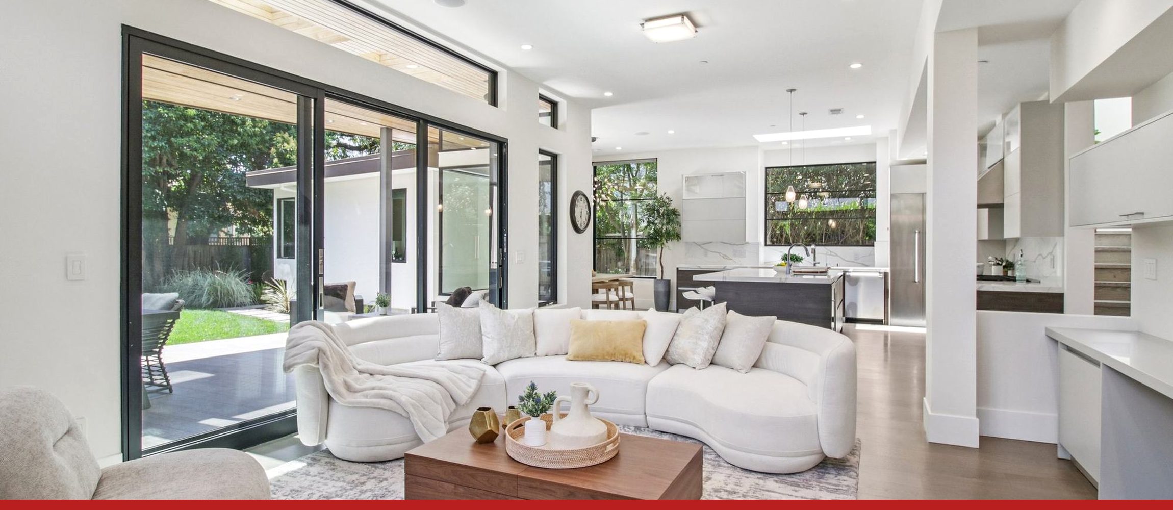 A bright living room opening onto its garden through a wall of glass, with the kitchen beyond