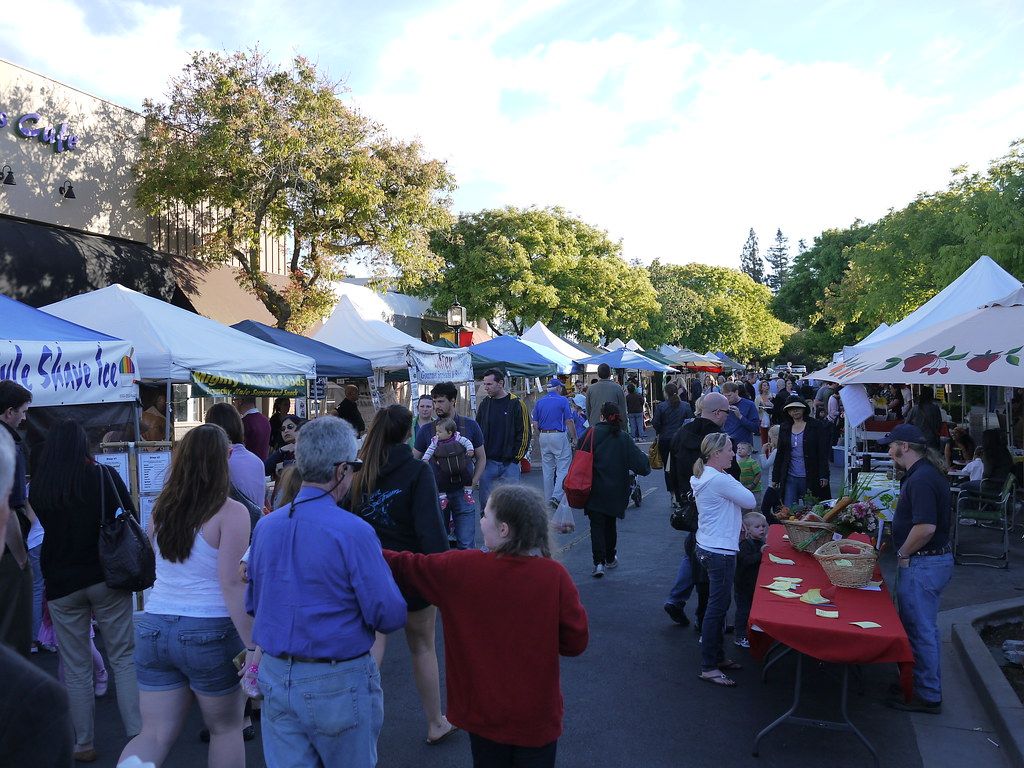 Shoppers walking between stalls at the Los Altos farmers’ market on a downtown street