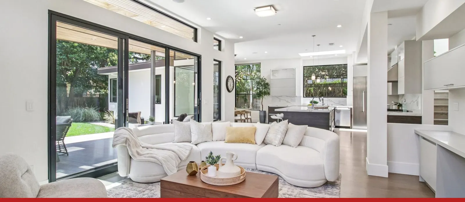 A bright living room opening onto its garden through a wall of glass, with the kitchen beyond
